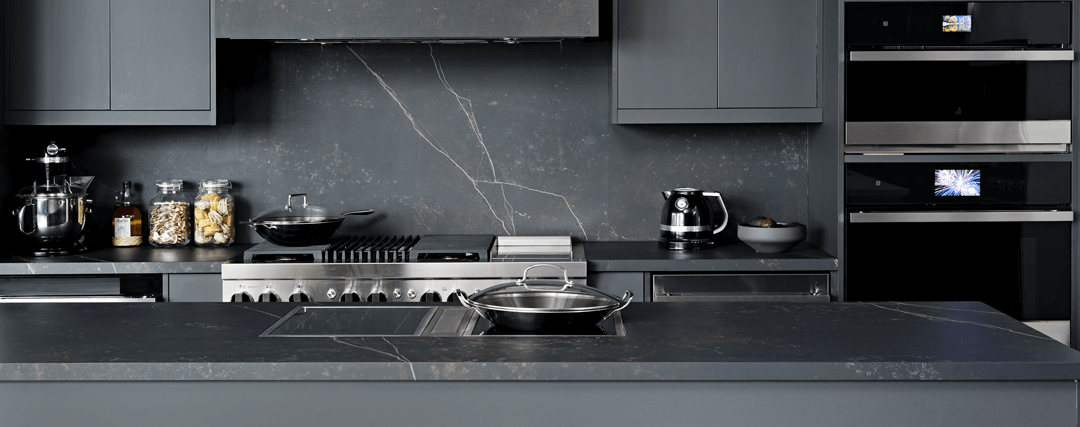 A JennAir Induction Cooktop installed in a dark, modern kitchen with other JennAir Brand appliances. 